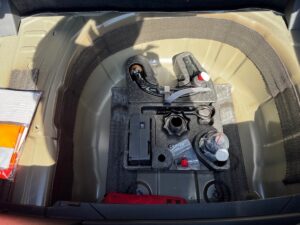 Kofferraumablage mit Werkzeugeinsatz in einem Auto, verschiedene Werkzeuge auf beigem Metallboden.