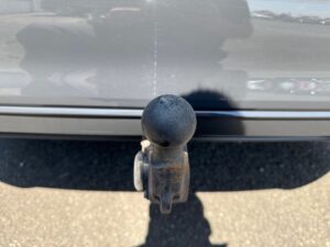 Anhängerkupplung hinten an einem grauen Auto, leicht rostige Koppelung, bei sonnigem Wetter.