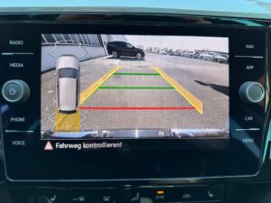 Rückfahrkamera-Ansicht mit Sicherheitslinien in Gelb, Rot und Grün, parkende Autos im Hintergrund.
