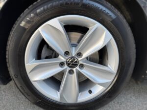 Silberne Autofelge, Reifenmarke Michelin, mit Volkswagen-Logo in der Mitte auf grauem Untergrund.