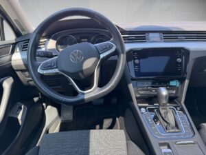 Innenraum eines Autos, mit schwarzem Lenkrad und Armaturenbrett, VW-Logo sichtbar.