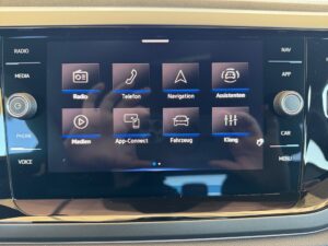 Nahaufnahme eines Autoinfotainmentsystems mit diversen App-Symbolen und glänzender Oberfläche.