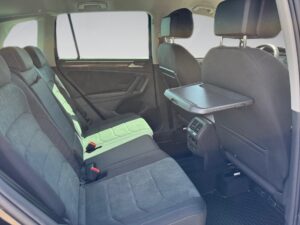 Zweireihige Autositze mit grauem Stoff, schwarze Details, klappbarer Tisch, moderne Innenausstattung.