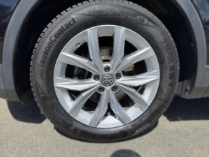 Silberne Volkswagen-Autofelge mit Allwetterreifen, klaren Speichen auf grauer Asphaltfläche.