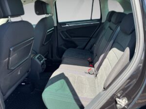 Schwarzes Auto, Innenraum hinten, graue Stoffsitze, helle Fenster, schwarze Türverkleidungen.