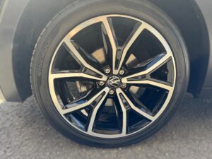 Ein schwarzes und silbernes Autoreifen mit komplexem Speichenmuster auf grauem Asphalt.