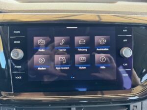 Bildschirm in einem Auto zeigt ein Infotainment-System mit verschiedenen App-Icons und Menüpunkten.