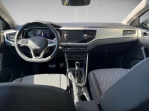 Innenraum eines modernen Autos mit grauen Sitzen und Lenkrad; hohe Bildschirme und silberne Akzente.