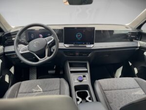 Auto-Innenraum mit digitalem Display, Lenkrad mit Logo, graue Sitze und schwarzes Armaturenbrett.