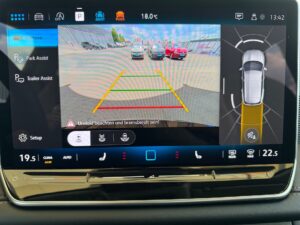 Farbige Rückfahrkameraansicht in einem Fahrzeugdisplay; mehrere Autos im Hintergrund sichtbar.