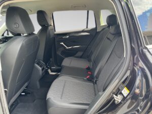 Schwarzer Autoinnenraum mit grauen Textilsitzen, klarer Himmel draußen, moderne Türdetails.