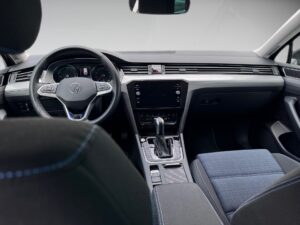 Innenraum eines Autos mit dunklem Lenkrad, grauem Armaturenbrett und blau-schwarzen Sitzen.
