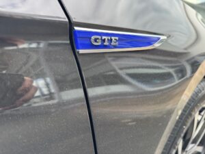 Schwarzes Auto mit blauem "GTE"-Emblem, glänzende und reflektierende Oberfläche, seitliche Ansicht.