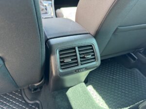 Hintere Autoventilatoren an schwarzer Konsole, umgeben von dunklen Polstern und Fußraum-Matten.