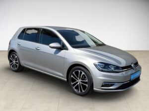 Silberner Volkswagen Golf in einem Studio, frontal leicht von der Seite fotografiert.