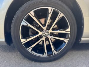 Reifen eines weißen Autos mit einer schwarzen und silbernen Felge von Volkswagen, auf Asphalt.