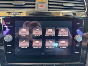 Ein Auto-Display zeigt Bedienelemente für Radio, Medien und Navigation in einem dunklen Farbschema.