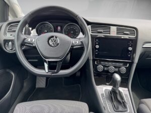 Innenraum eines VW-Autos mit Lenkrad, Tachometer, Infotainment-Bildschirm und Schalthebel in Grau.