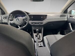 Auto-Innenraum mit schwarzem Armaturenbrett, Lenkrad, großem Bildschirm und manueller Schaltung.