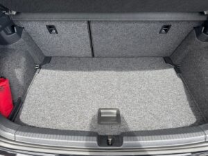 Kofferraum eines Autos mit grauem Teppichboden, leer außer rotem Notfallset in der linken Ecke.