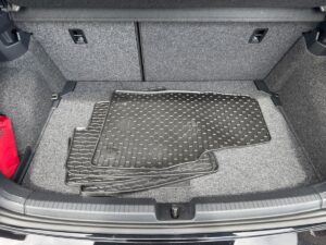 Kofferraum eines Autos mit Gummimatten auf grauem Teppich, eine rote Tasche links.