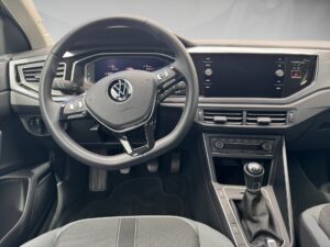 Innenraum eines Autos mit Volkswagen-Logo auf dem Lenkrad, graue und schwarze Details, moderner Look.