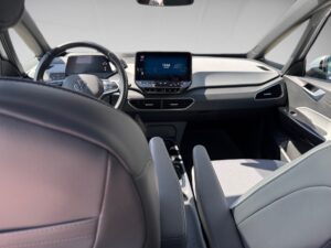 Innenansicht eines Autos, graue Sitze, Display zeigt Uhrzeit, Lenkrad links, modernes Design.