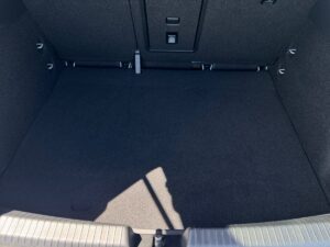 Leerer Kofferraum mit grauem Teppichboden, Schattenmuster am Boden, geraden schwarzen Wänden.