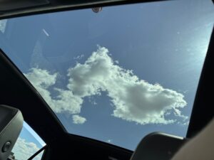 Blick durch ein Autodach auf blauen Himmel mit weißen Wolken; moderne Innenausstattung.