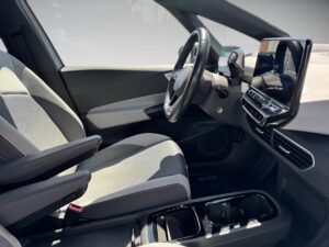 Innenansicht eines modernen Autos, graue Sitze, schwarzes Lenkrad, digitales Display.