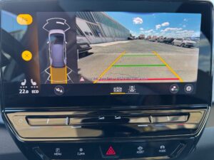 Farbdisplay eines Autos, zeigt Rückfahrkameraansicht und Umgebung mit Parkplatz und Gebäuden.
