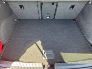 Kofferrauminnenraum eines Autos mit grauem Teppichboden und einem Lichteinfall von links oben.