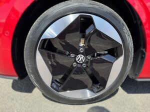 Nahaufnahme eines schwarzen, fünfspeichigen VW-Rads mit Reifen auf einer roten Karosserie.