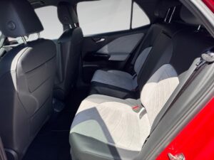 Rücksitze eines Autos mit hellgrauen Polstern, roten Türverkleidungen und schwarzem Interieur.