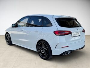Ein weißer Mercedes-Benz Kompaktwagen, Dreiviertelansicht von hinten, in einer hellen Umgebung.