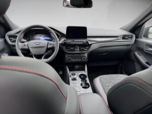 Innenraum eines Autos mit modernem Armaturenbrett und schwarzem Leder, roter Nahtdetail.