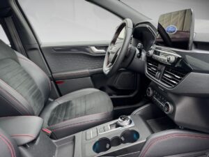 Innenraum eines modernen Autos mit schwarzem Interieur, roten Nähten und digitalem Display.