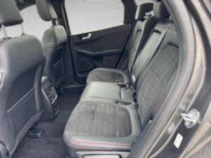 Innenraum eines schwarzen Autos mit Ledersitzen, roten Nähten und hinteren Lüftungsschlitzen.