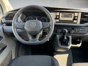 Innenraum eines Volkswagen Kastenwagens mit Lenkrad, Schalthebel und grauem Armaturenbrett.