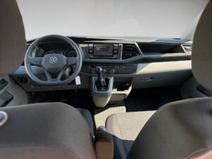 Innenansicht eines Autos mit grauem Armaturenbrett, Lenkrad mit VW-Logo, Schalthebel und Display.