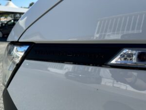 Weiße Fahrzeugfront mit "Transporter"-Schriftzug und reflektierenden Details.