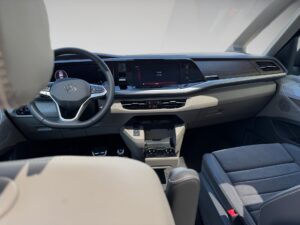 Innenraum eines modernen Autos, graue Sitze, großes Display, Lenkrad mit Markenlogo.