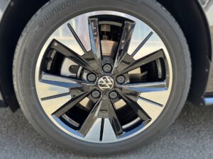 Ein schwarzer Autoreifen mit glänzender VW-Felge und fünf Doppelspeichen auf Asphalt.