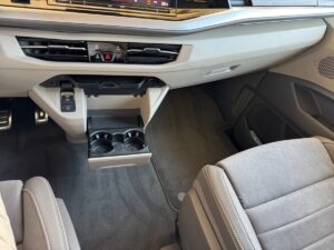 Innenraum eines Autos mit grauen Sitzen, Mittelkonsole und offener Getränkehalter-Schublade.