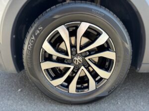Nahaufnahme eines silbernen Autoreifens mit modernem Felgendesign auf grauem Hintergrund.