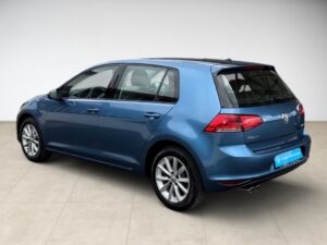 Blauer VW Golf von schräg hinten, helle Felgen, rote Rückleuchten, moderner Stil.