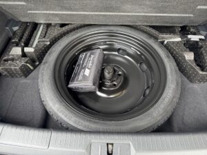 Reserverad und schwarzes Werkzeugset im Kofferraum eines Autos, silberfarbenes Abdeckfach.