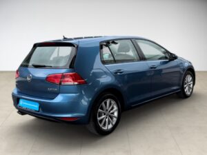 Ein blauer VW Golf 7 steht in einem hellen Raum, seitliche Heckansicht.