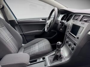 Innenraum eines Autos mit gestreiftem Sitz, schwarzem Armaturenbrett und Schalthebel.