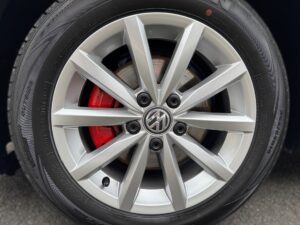 Autoreifen und silberne Felge mit roter Bremse und VW-Logo in der Radmitte.